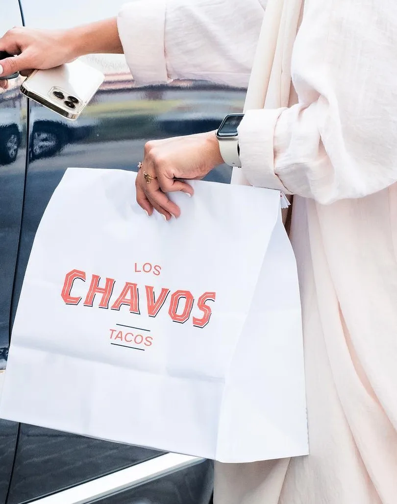 Bolsa blanca para llevar con el logotipo, en la mano de una persona junto a un coche.